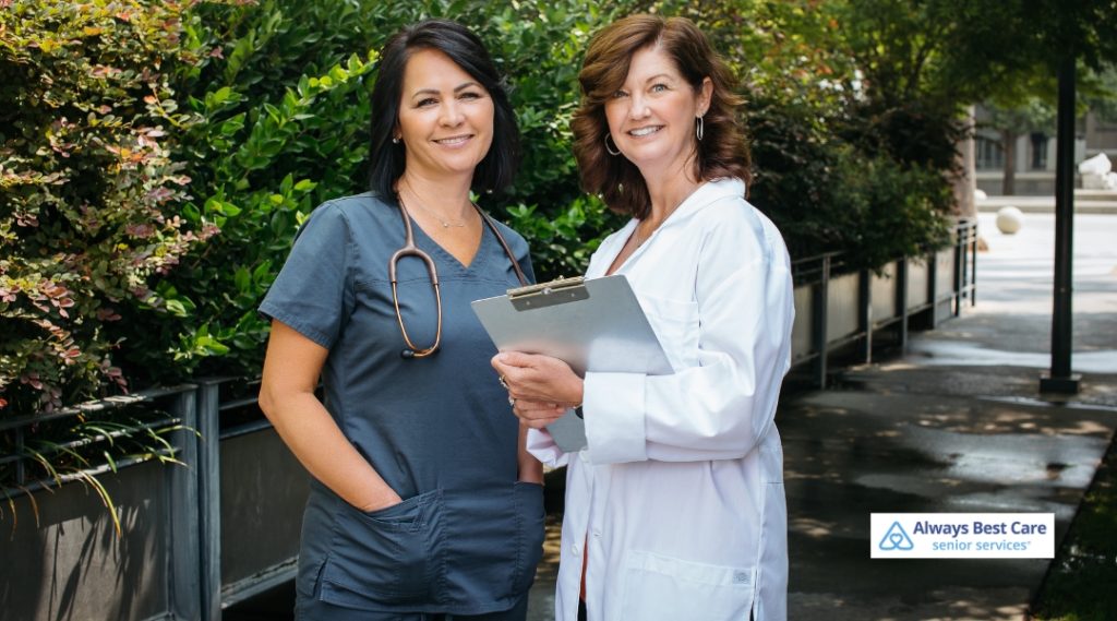 A caregiver and a medical professional from Always Best Care stand together outdoors, both smiling and ready to provide compassionate care.