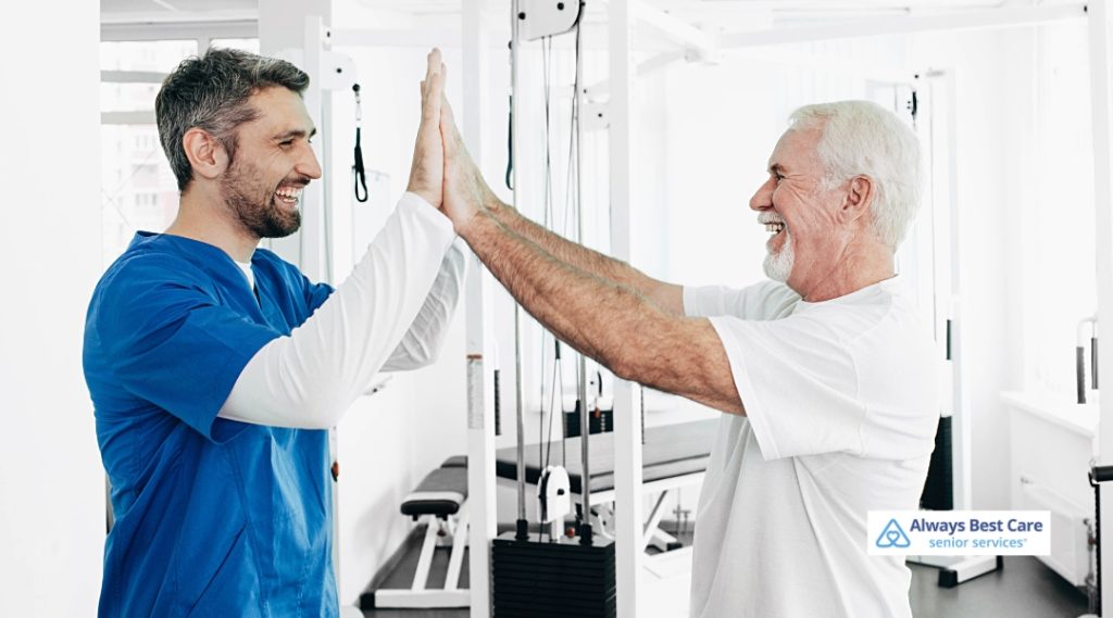 senior man and a caregiver in scrubs share a cheerful high-five during a rehabilitation session at a fitness facility.
