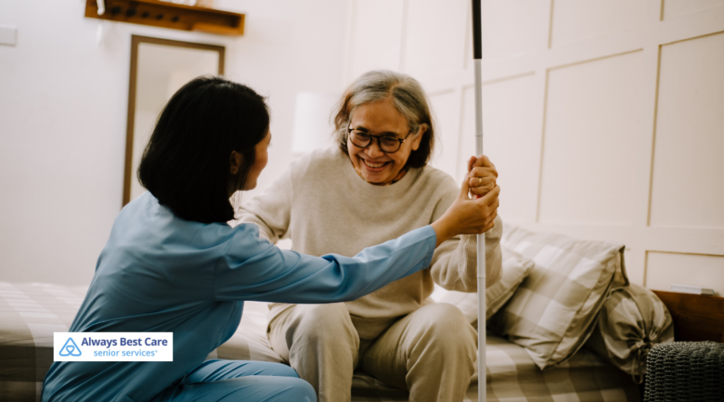 A caregiver helping an older woman sit up on her bed while smiling and providing support, emphasizing friendly in-home senior care.