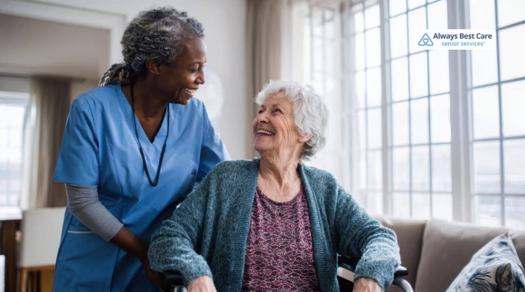 1. A caregiver smiles warmly at an elderly woman in a wheelchair, creating a moment of care and connection at home. The caregiver is dressed in blue medical attire. 2. Image 2: A caregiver and an elderly woman share a heartfelt moment together, smiling at each other with a supportive and comforting atmosphere at home. The caregiver is dressed in blue medical clothing.
