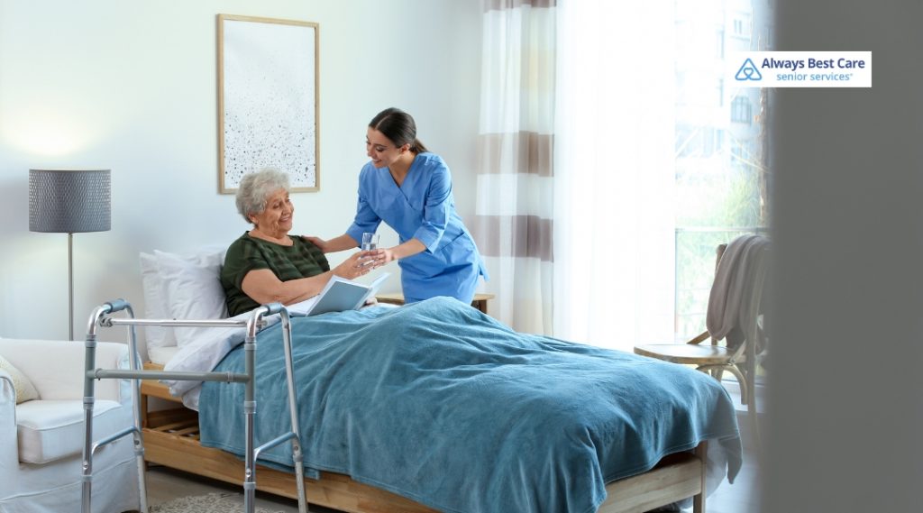 Caregiver in blue scrubs offers a glass of water to an older woman 