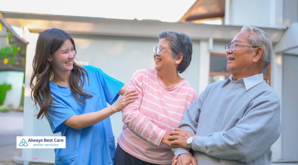 Caregiver laughs with an older couple outdoors.
