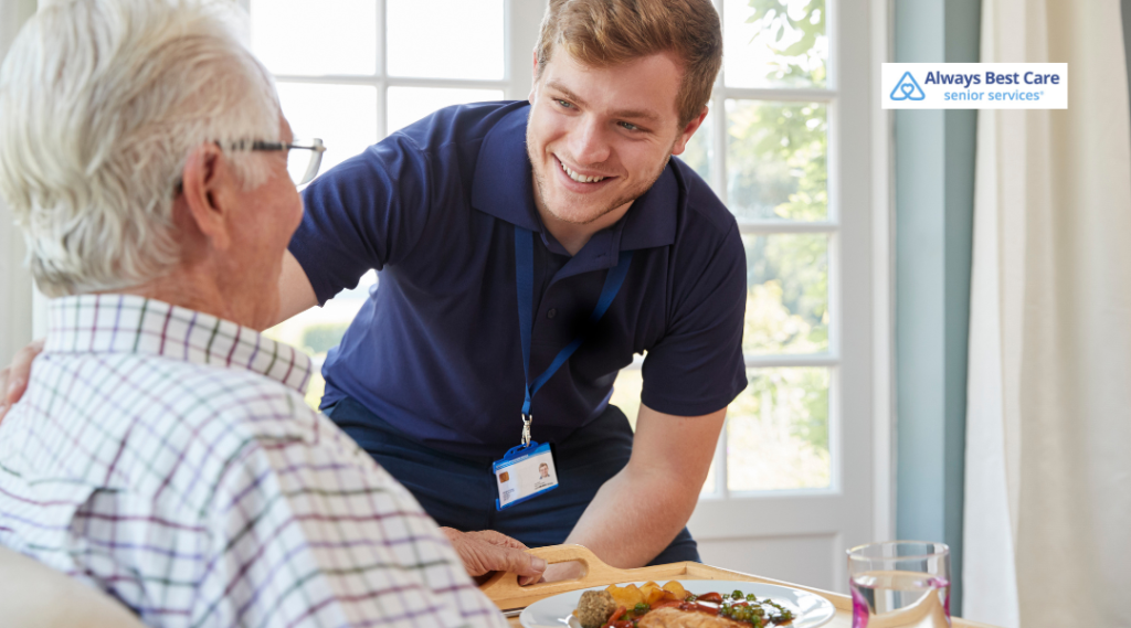 Caregiver serving a meal and speaking with an older man at home.