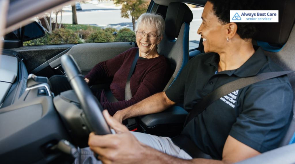Always Best Care caregiver drives a smiling senior woman, and they chat and laugh in the front seats of a car.