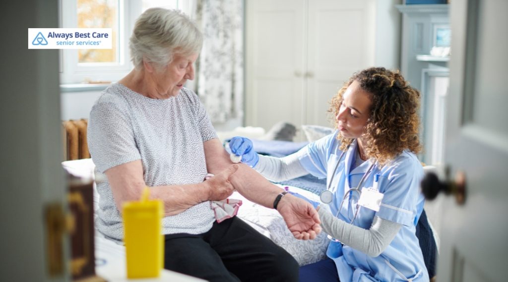 A caregiver in blue scrubs prepares to administer a medical procedure to an elderly woman by taking her blood, providing compassionate care in a well-lit room.