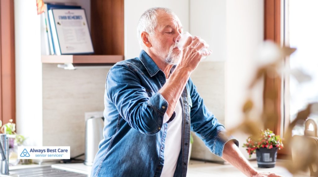 Senior man enjoying a refreshing glass of water in the kitchen with a relaxed expression.