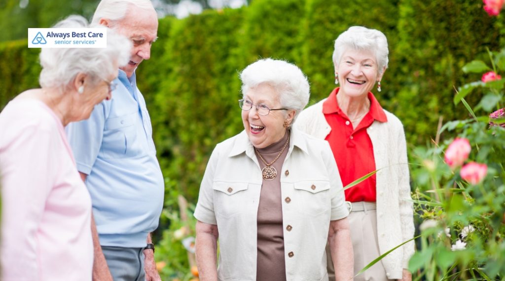 Four older adults smiling and socializing together in a lush garden.