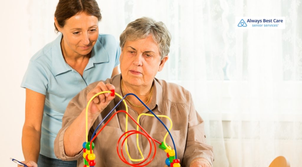 A caregiver assists an elderly woman using a bead maze toy for cognitive stimulation.