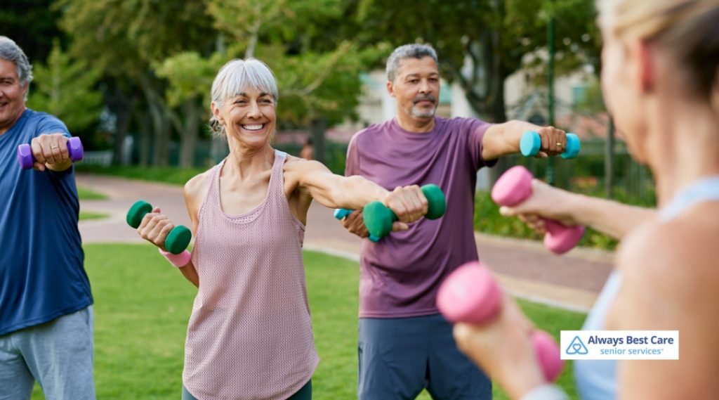 Group of older adults smiling and doing light strength exercises with colorful dumbbells in a park.