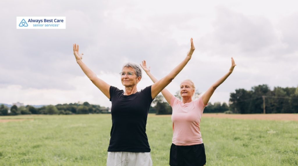 Two older women standing in a field with arms raised, doing gentle outdoor exercise.