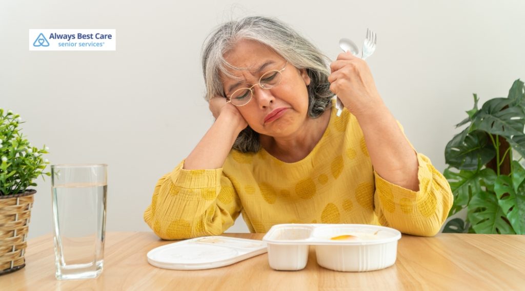 Frustrated elderly woman stares at an unappetizing microwaved meal, representing the challenges of senior nutrition when support is lacking.