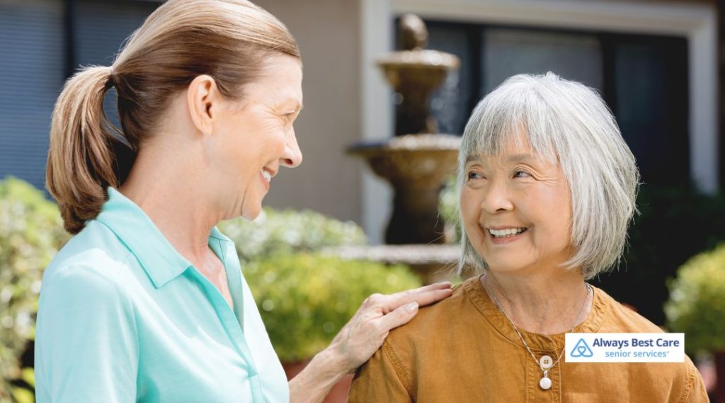 An Always Best Care Senior Services caregiver offering reassurance and support to a senior woman outdoors, with a garden fountain in the background, illustrating compassionate in-home care.