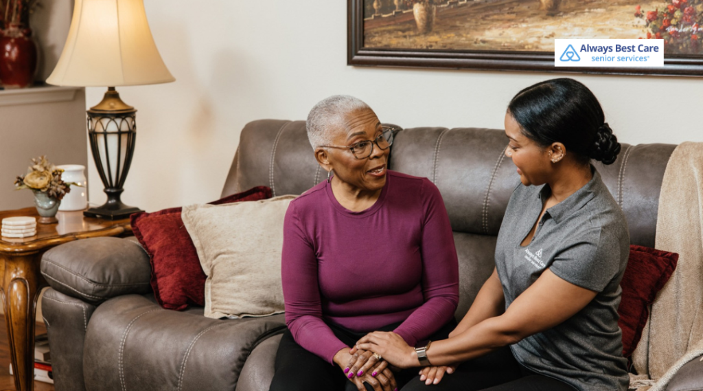 Caregiver sitting beside a senior woman on a couch, offering support and friendly conversation.