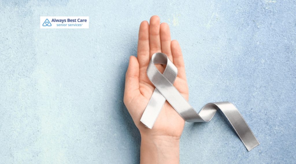 A silver awareness ribbon, representing Parkinson’s Disease, rests in the palm of an open hand against a light blue textured background, symbolizing advocacy and support.