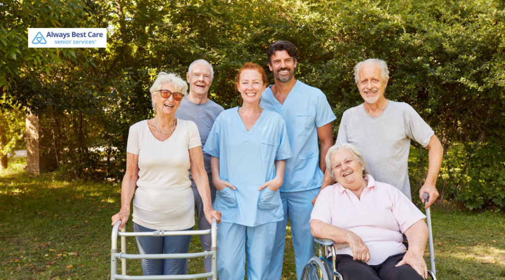 Group of seniors and caregivers smiling together outdoors, showing companionship and supportive care.