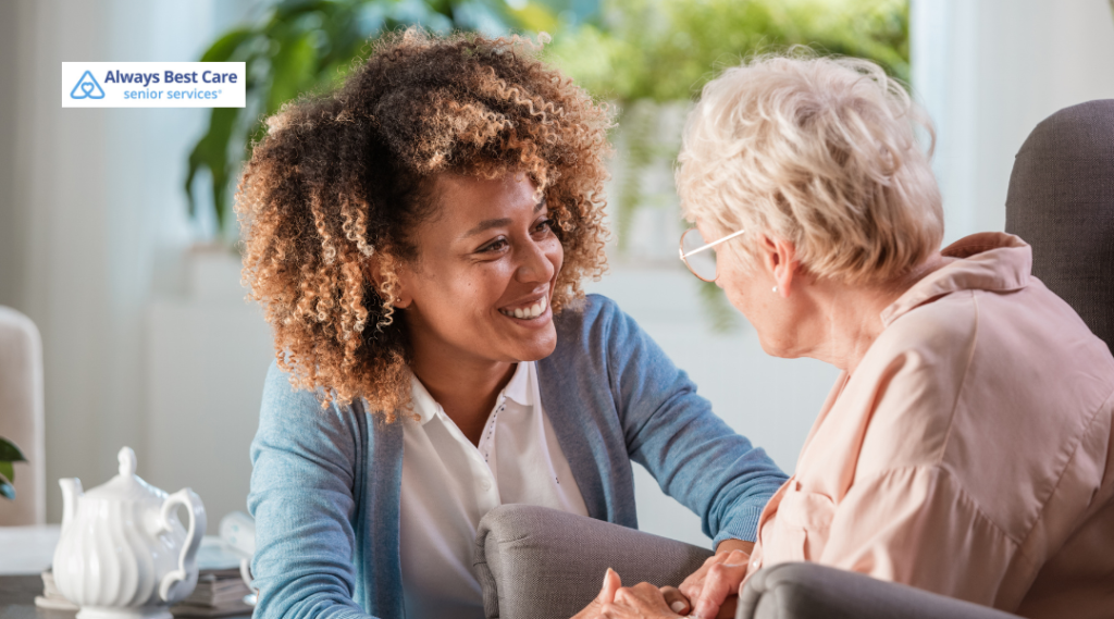 Caregiver holding hands and talking with an older woman at home.