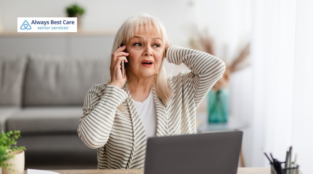 Senior woman holding the phone to her ear in shock in front of a laptop