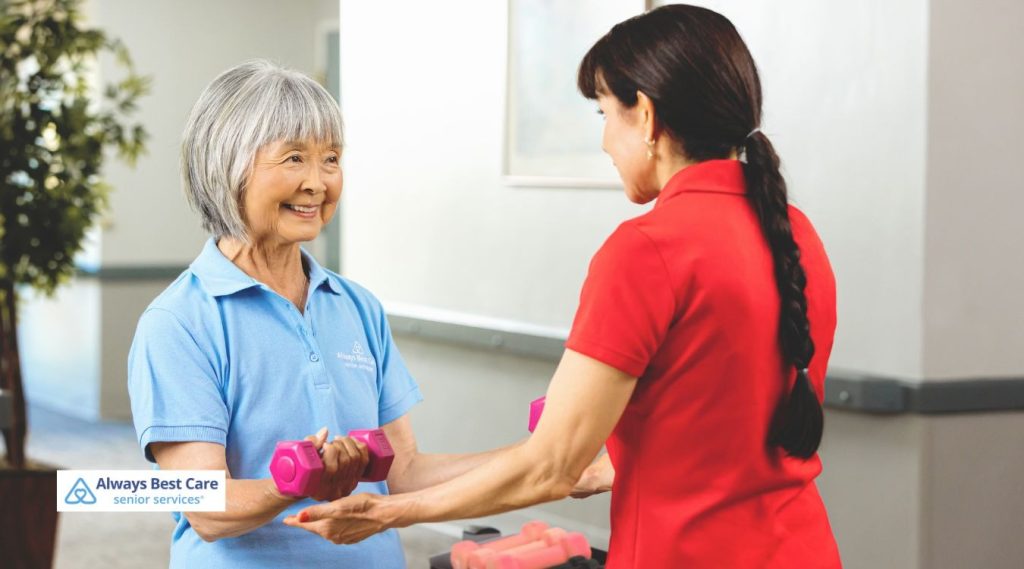 A health care provider assists an elderly women to excercise with pink weights