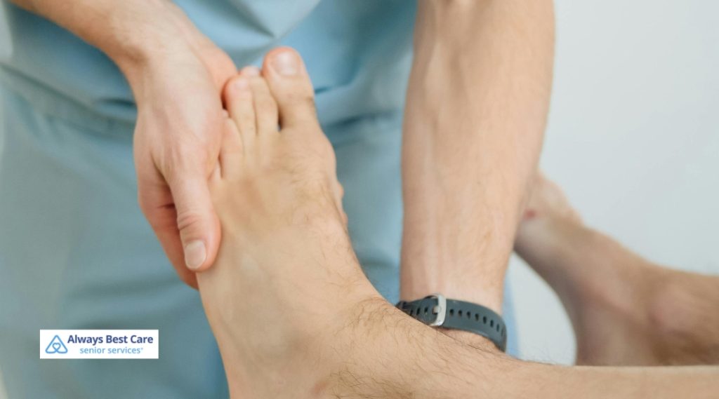 A healthcare professional in light blue scrubs holds and carefully examines a patient's bare foot, providing care or assessment of the lower limb.