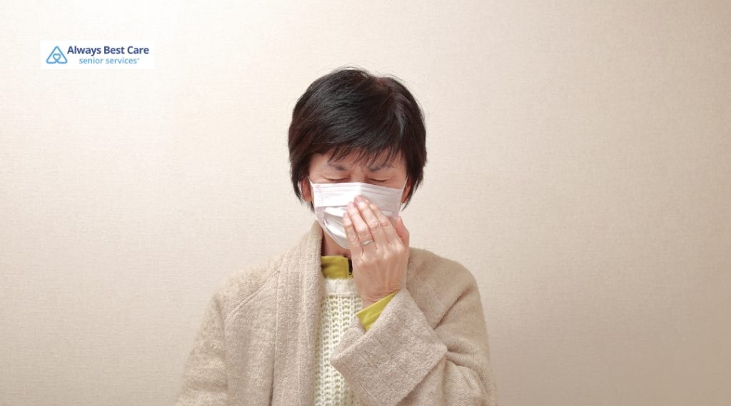 Woman wearing a face mask and covering her mouth while standing indoors, appearing unwell.