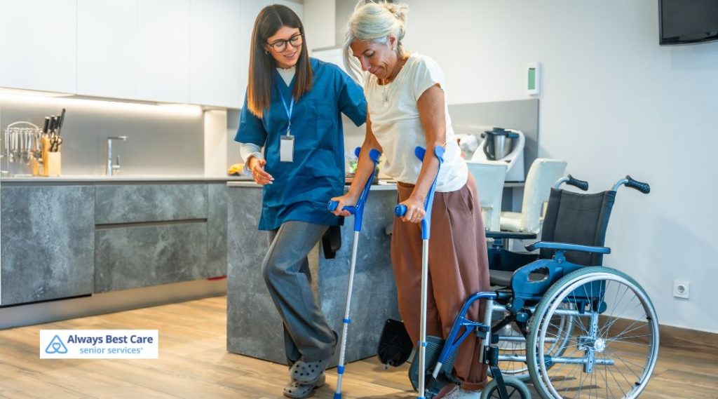 "A caregiver assisting a senior woman with crutches, walking in the kitchen area. The caregiver is providing physical support, ensuring the senior's safety while moving around the home.