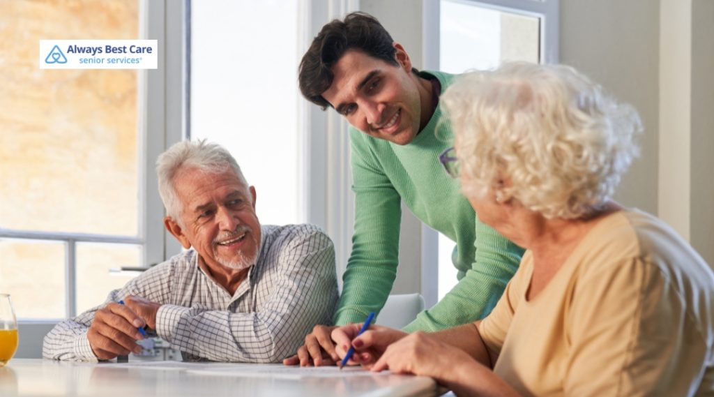 Two elderly adults smiling and engaged in a memory care activity, with their caregiver providing assistance and companionship.