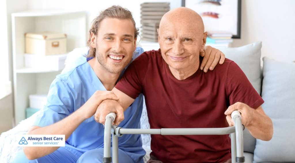 A caregiver and senior man smiling together in a comfortable home setting. The caregiver is helping the senior with a walker, demonstrating compassionate support and guidance in mobility."