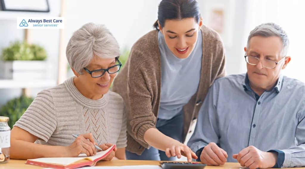 Caregiver helps an older couple budget, pointing at a calculator while they take notes.