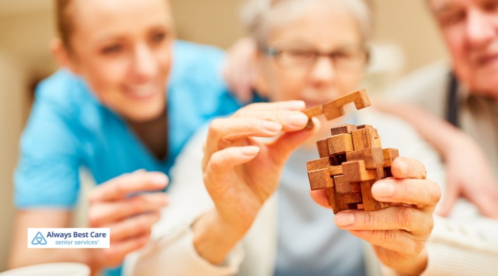 Senior woman engaging in a brain-stimulating wooden puzzle activity with a caregiver smiling in the background.