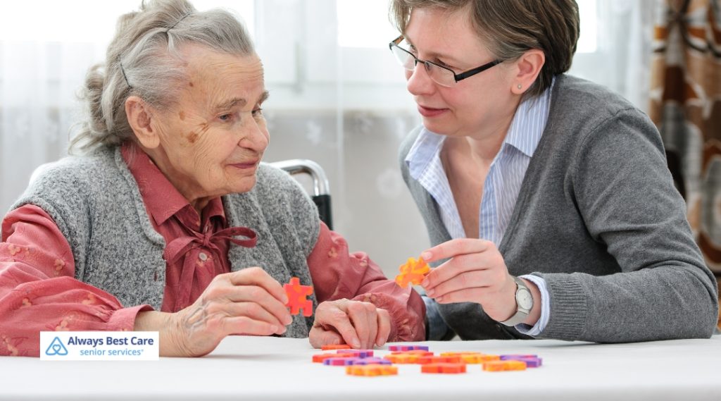 Elderly woman and a caregiver working together on a colorful puzzle game at a table.