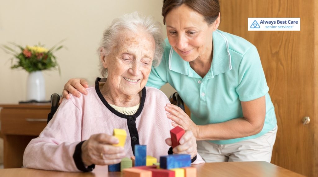 An elderly woman enjoys a moment of connection with her caregiver as they engage in a fun and interactive activity using colorful blocks, promoting cognitive engagement.