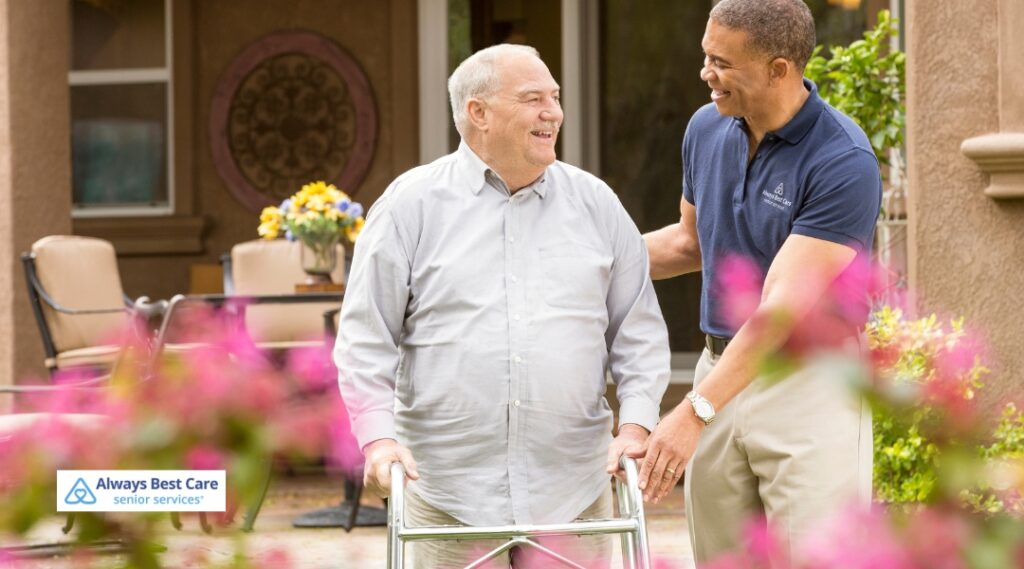 Caregiver helping a senior man walk safely with his walker on a sunny patio
