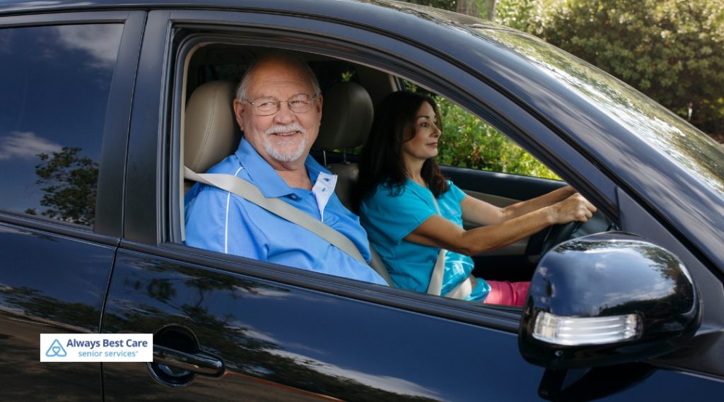 Older man rides in the passenger seat while a caregiver drives a car, both wearing seatbelts