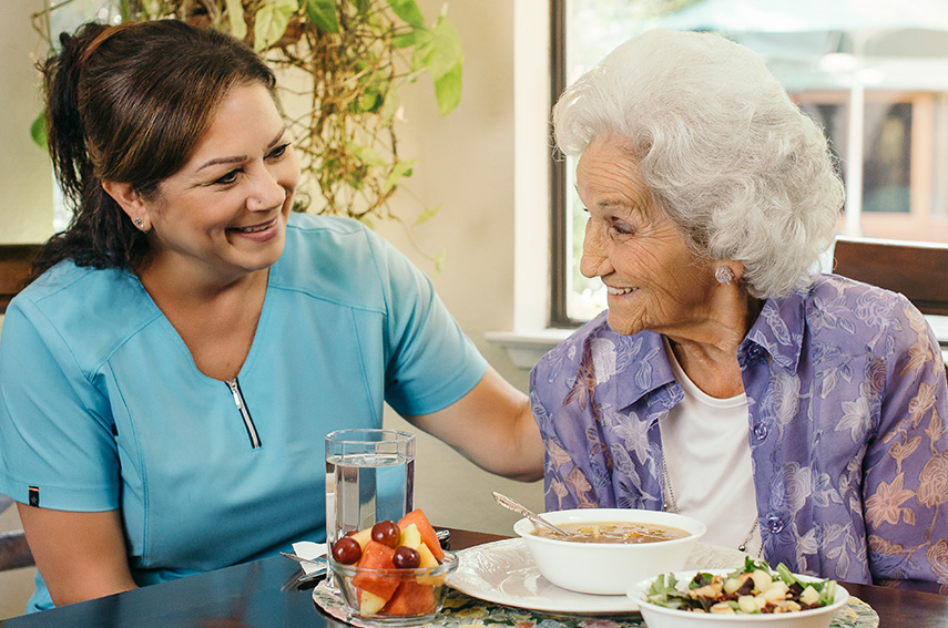 A CAREGIVER ASSISTING SENIOR WOMAN WHILE EATING