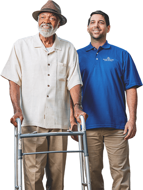 SMILING SENIOR IN WALKER GUIDED BY CAREGIVER