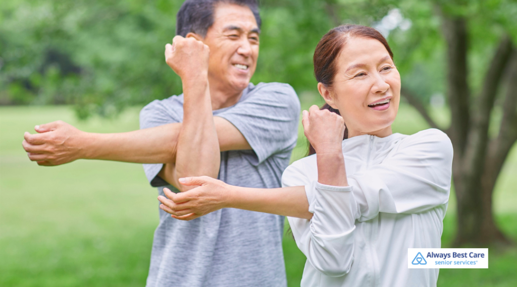 Older couple stretching their arms together outdoors, practicing gentle exercise to support heart health and mobility.