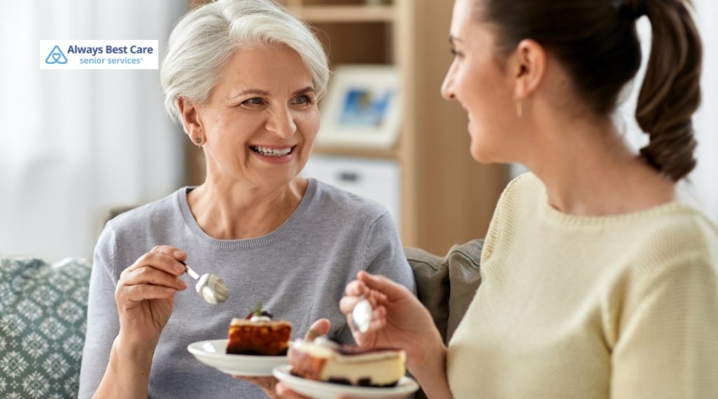 An older woman and a younger woman share a joyful moment over dessert, highlighting companionship and emotional well-being.