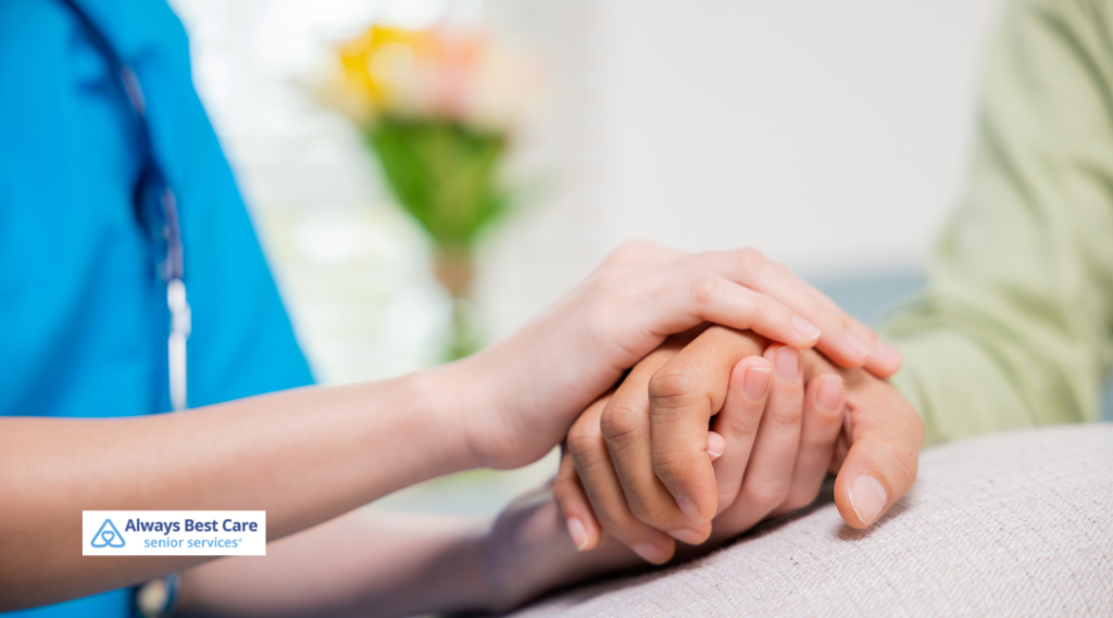 A caregiver gently holding a senior’s hand in a comforting indoor setting, symbolizing compassion and support in senior home care.