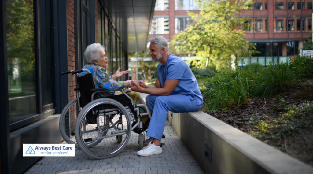 A caregiver kneeling beside a senior woman in a wheelchair outdoors, sharing a warm conversation in a peaceful garden setting.