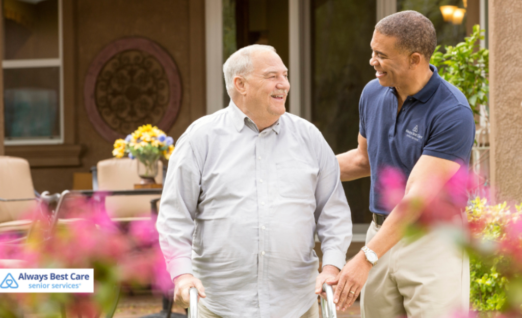 A caregiver supports a smiling senior man with a walker outdoors, reflecting safe, encouraging, and dignified mobility assistance from Always Best Care of Nashville.