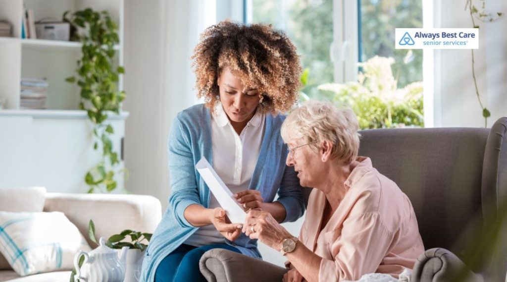 Smiling caregiver showing documents to an older woman in a bright living room, offering friendly support and guidance.