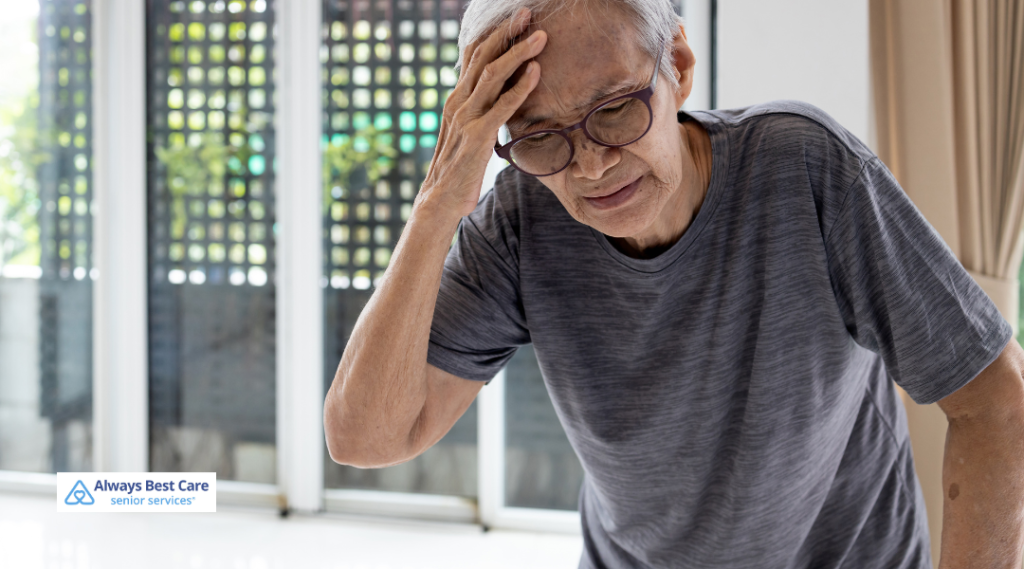 Older woman leaning forward and holding her head, showing signs of dizziness or balance difficulty inside her home.