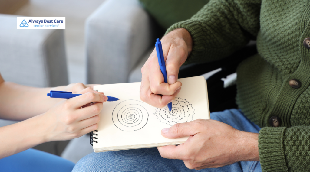 Two people draw spiral patterns in a sketchbook using blue pens; ‘Always Best Care senior services’ logo in the corne