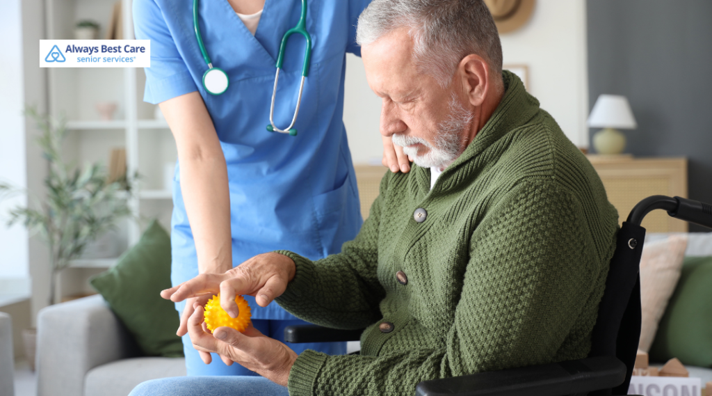 Caregiver with a stethoscope supports an older man seated in a wheelchair as he squeezes an orange spiky therapy ball; ‘Always Best Care senior services’ logo in the corner.