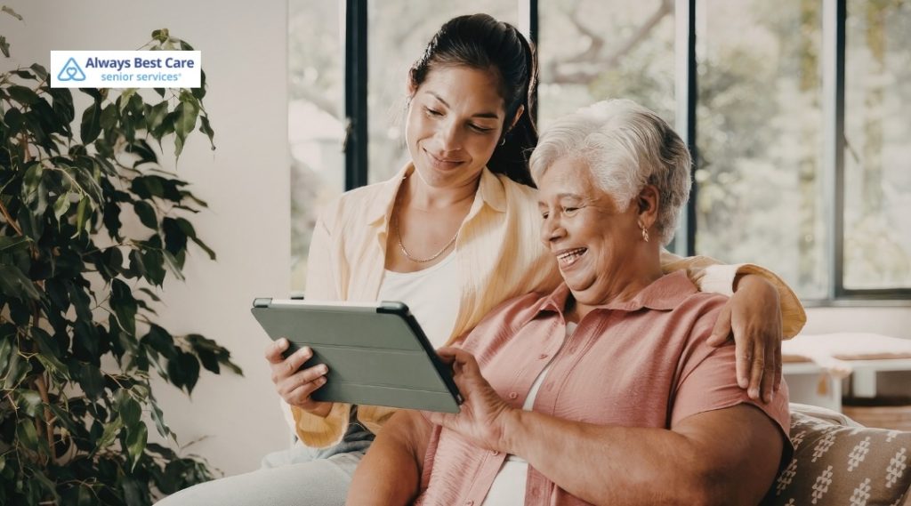 SENIOR SCAMS: HOW TO RECOGNIZE THE WARNING SIGNS AND PROTECT YOUR LOVED ONE IN HOLLYWOOD, FL 6 HAPPY SENIOR WOMAN SITTING WITH A CARING COMPANION, SMILING WHILE LOOKING AT A TABLET TOGETHER AT HOME.