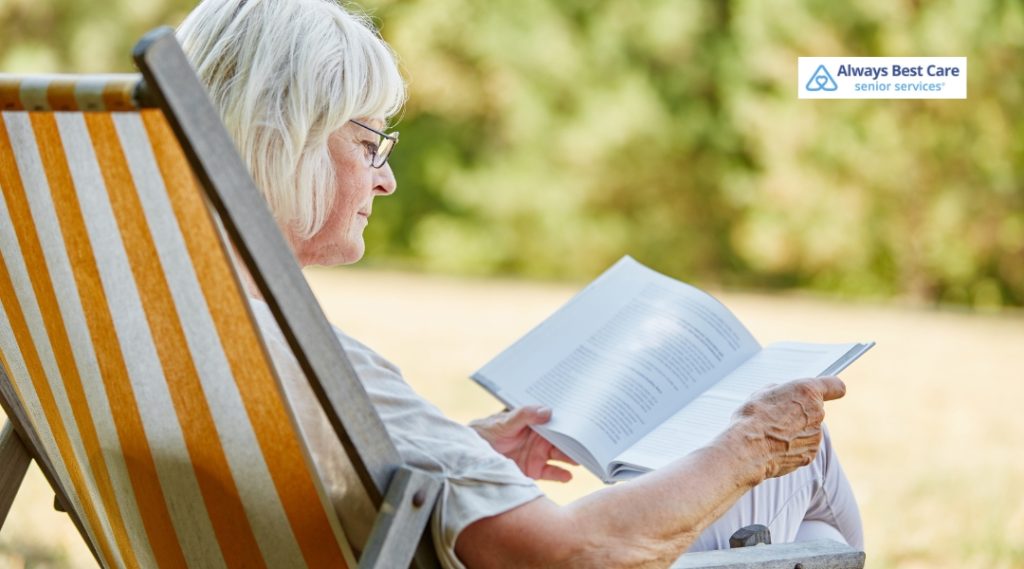  SENIOR WOMAN READING A BOOK WHILE RELAXING IN AN OUTDOOR CHAIR.