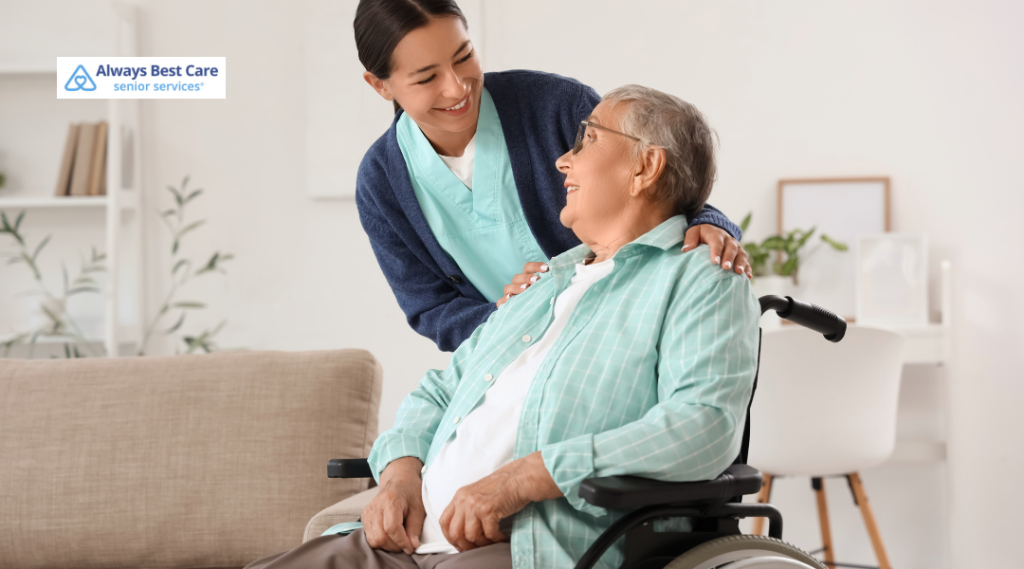 Smiling caregiver comforting an older man seated in a wheelchair at home.