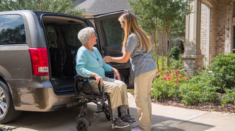 caregiver helping a senior woman in a wheelchair exit a transport van outside a home, reflecting supportive senior care sugar land, tx