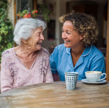 Caregiver and senior woman smiling together over coffee, showing companionship and daily support through home care in Houston, TX.