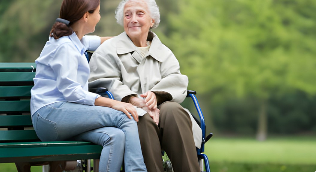 Compassionate caregiver sitting with senior woman in wheelchair outdoors, providing home care support